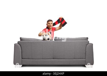 Junger Fußballfan jubelt auf einem grauen Sofa isoliert auf weißem Hintergrund Stockfoto
