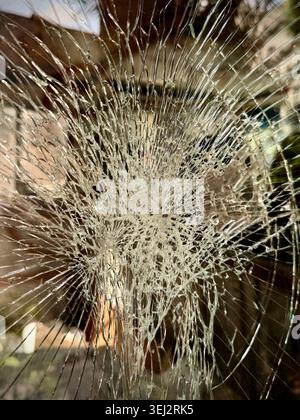 Nahaufnahme eines zersplitterten Glases mit einem Spinnennetz-Rissmuster, das auf Schäden, Aufprall, Fragilität und Verwundbarkeit in der Stadt hindeutet Stockfoto