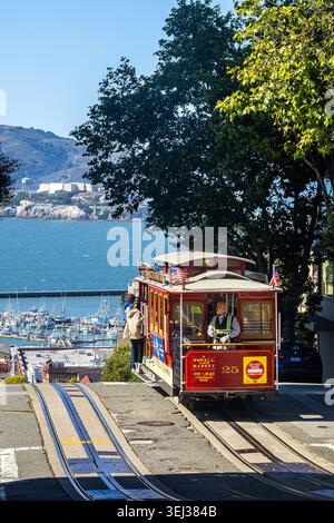 Die San Francisco Cable Car fährt auf Schienen auf einem steilen Hügel mit Blick auf Alcatraz Island, SF Bay Area berühmte Straßenbahn Transport Stockfoto