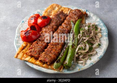 Traditionelles türkisches Adana Kebab auf Fladenbrot mit gegrilltem Gemüse und Zwiebelsalat Stockfoto