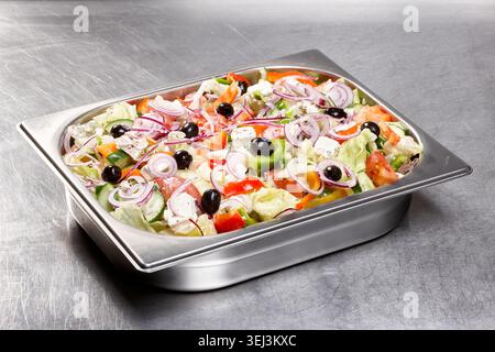Ein lebhafter Gartensalat mit einer Mischung aus knusprigem Salat, frischen Tomaten, geschnittenen Zwiebeln und Oliven, die mit Dressing getränkt werden, wird in einem Metallrestaurant serviert Stockfoto