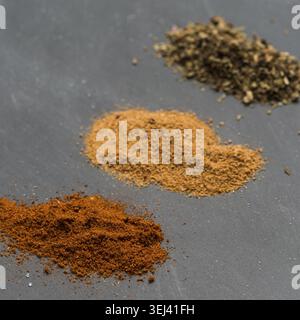 Drei verschiedene bunte Pulvergewürze, kleine Stapel auf schwarzem Tafel-Hintergrund Stockfoto