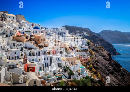 Farbenfrohe und weiß getünchte Gebäude kaskadieren die Caldera-Klippen von Oia, Santorin, mit Blick auf die Ägäis in Griechenland. Stockfoto