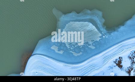 Luftgefrorener Teich und schneebedeckte Landschaft Top-Down-Winter-Abstract Stockfoto