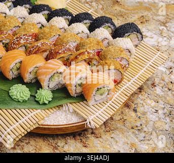 Essen, Eine bunte Auswahl an Sushi-Brötchen, ordentlich auf einer Bambusmatte angeordnet. Die Platte enthält verschiedene Arten von Brötchen mit frischem Fisch und Gemüse Stockfoto