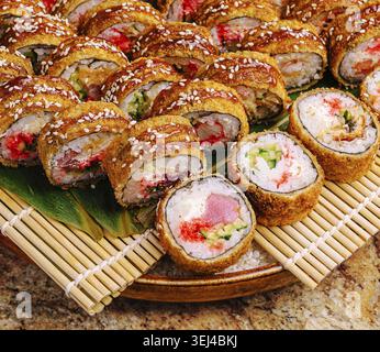 Essen, Eine Vielzahl von Sushi-Brötchen wird ordentlich auf einer Holzplatte mit Bambusmatte darunter gelegt. Die farbenfrohen Brötchen enthalten verschiedene Zutaten und Stockfoto