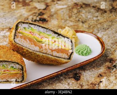 Food, Ein köstliches Sushi-Brötchen, besteht aus Schichten frischen Lachs, Krabben und Gemüse, umhüllt von einer knusprigen, frittierten Außenschicht. Garniert mit Wasabi und p Stockfoto