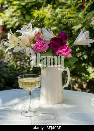 Ein Coupé-Glas Sekt oder Champagner, serviert im Freien auf einem sonnigen Tisch mit weichem Gartenhintergrund. Stockfoto