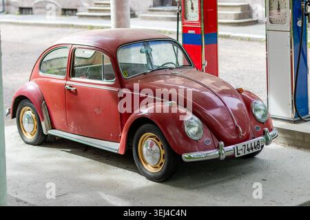Roter Volkswagen Käfer Typ 1, der neben Retro-Kraftstoffpumpen an einer alten Tankstelle in Norwegen geparkt wurde Stockfoto