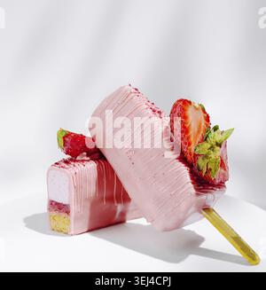 Essen, zwei leuchtend rosa Eiscremepops stehen auf der Ausstellung, gekrönt mit frischen Erdbeeren. Die Einstellung ist einfach und konzentriert sich auf die farbenfrohe Leckerei Stockfoto
