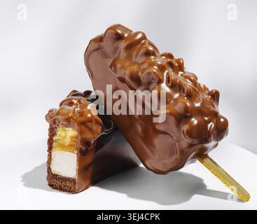 Essen, Nahaufnahme von zwei mit Schokolade überzogenen Eisriegeln, die auf einer weißen Oberfläche liegen und eine knusprige Beschichtung und eine cremige Füllung aufweisen. Das Leckerli ist Appay Stockfoto