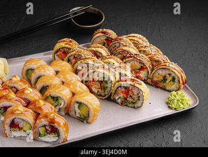 Essen, Eine Sushi-Platte bietet eine Vielzahl von Brötchen, einschließlich Lachs und frittierte Optionen. Farbenfrohe Saucen und Garnituren sorgen für einen optischen Reiz, m Stockfoto