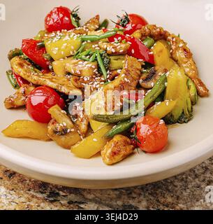 Speisen, Ein lebhaftes Pfannengericht mit zarten Hähnchenstückchen und verschiedenen Gemüsesorten wie Paprika, Kirschtomaten und grünen Bohnen. Das Gericht ist Stockfoto