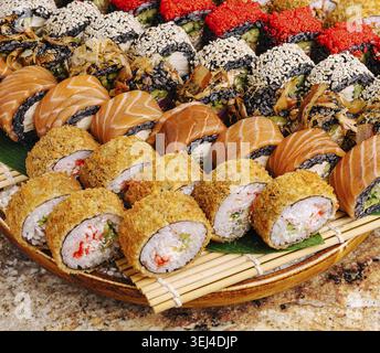 Essen, Eine bunte Auswahl an Sushi-Brötchen ist auf einem großen Holztablett angeordnet. Verschiedene Arten von Sushi, einschließlich knuspriger und traditioneller Brötchen, sind p Stockfoto