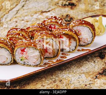 Das Essen, köstliche Sushi-Brötchen mit Krabbenfleisch und Sesam werden attraktiv serviert. Die Brötchen werden auf einer Holzplatte mit Ingwer serviert, Stockfoto