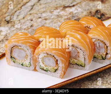 Das Essen, köstliche Nigiri-Sushi-Brötchen mit frischem Lachs und knuspriger Krabbenfüllung sitzen auf einem weißen Teller. Das Ambiente ist ein warmes Restaurant, perfec Stockfoto