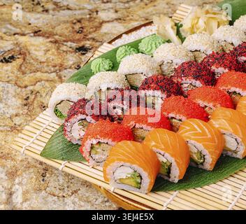 Speisen, bunte Sushi-Brötchen sind kunstvoll auf einem Bambustablett mit frischem Grün und Beilagen angeordnet. Die Platte bietet eine Vielzahl von Geschmacksrichtungen, Showcasi Stockfoto