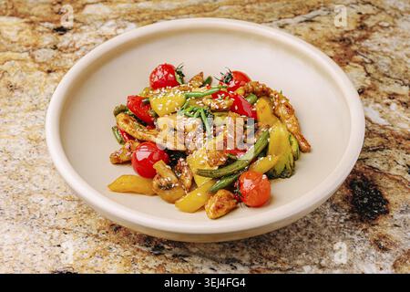 Speisen, Ein lebendiges Gericht aus gebratenem Huhn und verschiedenen Gemüsesorten, werden in einer tiefen Schüssel serviert. Die Mahlzeit umfasst Paprika, Kirschtomaten und s Stockfoto