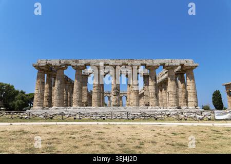 Capaccio Paestum - Kampanien - Italien - 07-06-2025: Vorderansicht eines antiken Steintempels mit großen Säulen im Sonnenlicht auf trockenem Grasland, begrenzt Stockfoto