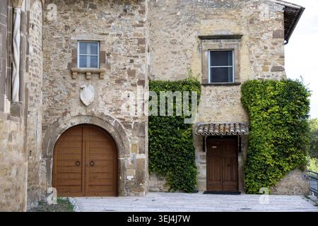 Vieste - Apulien - Italien - 08-29-2025: Verwitterte Steinfassade mit einem bogenförmigen Holztor, Efeu-bedeckte Wand, kleine Holztür unter einer gefliesten Markise und Stockfoto