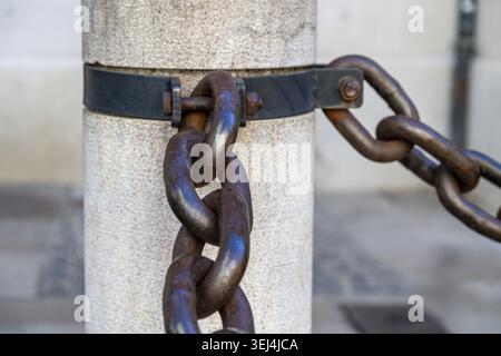 Eine große, schwere Metallkette sichert einen Steinpfosten und zeigt Details von altem Metall und Bolzen Stockfoto