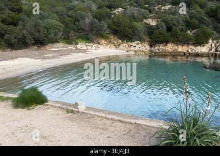 Eine kleine abgeschiedene Bucht mit Sandstrand, felsiger Küste und kristallklarem türkisfarbenem Wasser, umgeben von dichter grüner Vegetation Stockfoto