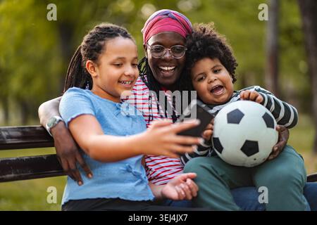 Glückliche Familie, die Selfie mit einem Kind macht, das im Park Fußball hält Stockfoto