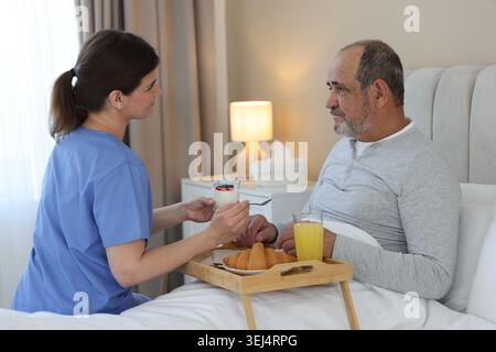 Die Pflegekraft frühstückt einem älteren Mann zu Hause im Bett Stockfoto
