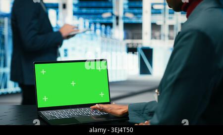 Green-Screen-Laptop, der von Softwareentwicklern für Rechenzentren verwendet wird, die AR-Simulation zur Überwachung von Systemen verwenden. Server-Hub-IT-Profi mit Chroma Key-Notebook für Optimierungen, VFX-Overlay, Kamera B Stockfoto