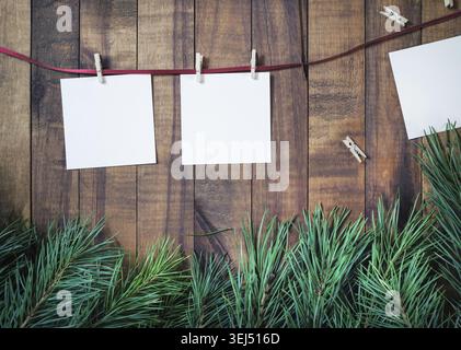 Leeres Fotopapier wird mit Wäschespins und Fichtenzweigen auf hölzernem Hintergrund am Seil befestigt Stockfoto