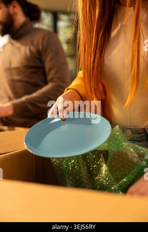 Nahaufnahme einer Frau, die in Kartons verpackte Haushaltsgegenstände auspackt, um sich in ihrem neuen Haus niederzulassen. Die Leute arrangieren Möbel und Dekorationen nach dem Umzugstag, dem Leben Ereignis. Stockfoto