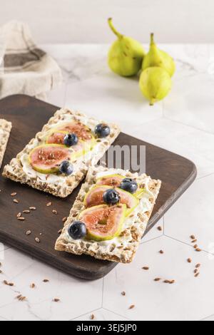 Canape oder Crostini mit mehrkörnigem Cristiaufstrich mit Frischkäse und frischen Feigenscheiben auf einem Holzbrett. Köstliche Vorspeise, ideal als Aperitif Stockfoto