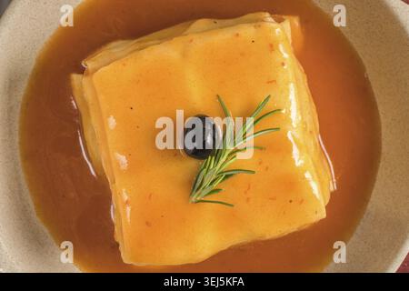 Traditionelle portugiesische snack Essen. Francesinha Sandwich-Brot, Käse, Schweinefleisch, Schinken, Wurst, Tomaten-Bier-Sauce und Pommes Frites. Mit Bier und Stockfoto