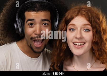 Aufgeregt, junges Paar, das gemeinsam Musik hört und Kopfhörer mit lockigem Haar trägt Stockfoto