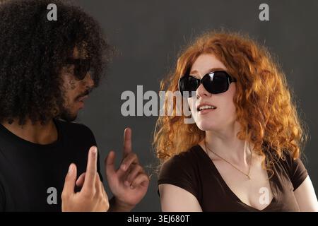 Junge, vielfältige Paare, die sich ausdrucksstark mit einer stilvollen Sonnenbrille austauschen Stockfoto