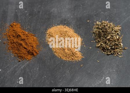 Drei verschiedene bunte Pulvergewürze, kleine Stapel auf schwarzem Tafel-Hintergrund Stockfoto