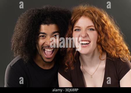 Glückliches junges gemischtes Paar lacht und lächelt breit vor Begeisterung Stockfoto