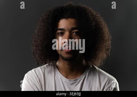 Junger Mann mit lockigen Afro-Haaren im Studio, der den Betrachter direkt ansieht Stockfoto