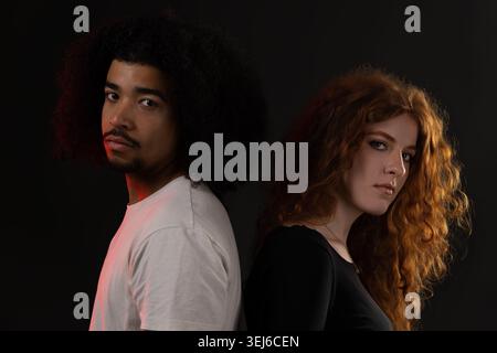 Verschiedene junge Paare stehen vor dunklem Hintergrund zurück und zeigen Beziehungsschwierigkeiten Stockfoto