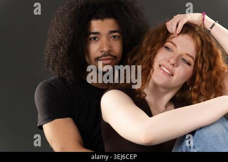 Ein junger Mann, der eine rothaarige Frau mit lockigen Haaren umschließt und ein liebenswertes, vielfältiges Paar repräsentiert Stockfoto