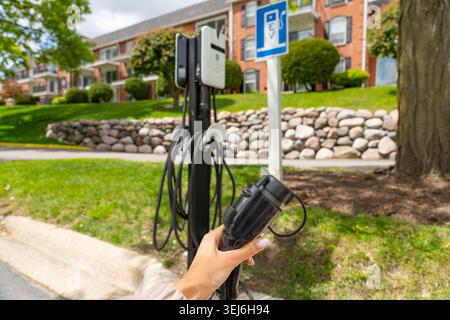 Eine Ladestation für Elektrofahrzeuge (EV) in einem Wohngebiet mit einer Hand, die einen EV-Ladestecker hält, Konzept steigender Kraftstoffpreise Stockfoto