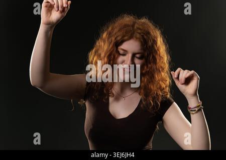Rothaarige Frau, die mit geschlossenen Augen und erhobenen Händen Freude ausdrückt Stockfoto
