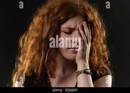 Eine junge Frau, die ihr Gesicht bedeckt und starke Emotionen wie Stress, Traurigkeit und Trauer erlebt Stockfoto