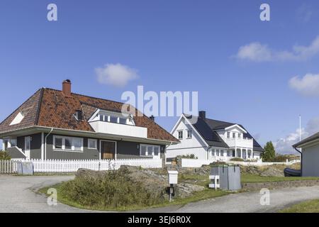 Helle schwedische Küstenhäuser auf der Insel Stora Dyron an der Küste von Tjorn, Schweden, mit roten Ziegeldächern und weißen Zäunen unter klarem blauen Himmel Stockfoto