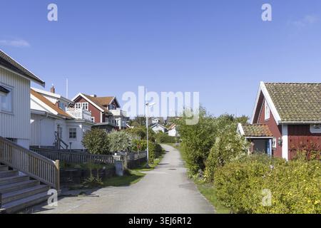 Helle schwedische Küstenhäuser auf der Insel Stora Dyron an der Küste von Tjorn, Schweden, mit roten Ziegeldächern und weißen Zäunen unter klarem blauen Himmel Stockfoto