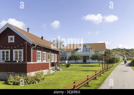 Helle schwedische Küstenhäuser auf der Insel Stora Dyron an der Küste von Tjorn, Schweden, mit roten Ziegeldächern und weißen Zäunen unter klarem blauen Himmel Stockfoto