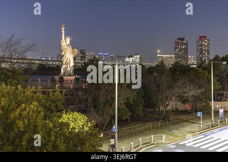 Tokio, Japan - 14. März 2025: Erleuchtete Odaiba Freiheitsstatue eine Nachbildung der Originalstatue in New York in der Nähe der Rainbow Bridge mit Blick auf die Brücke Stockfoto