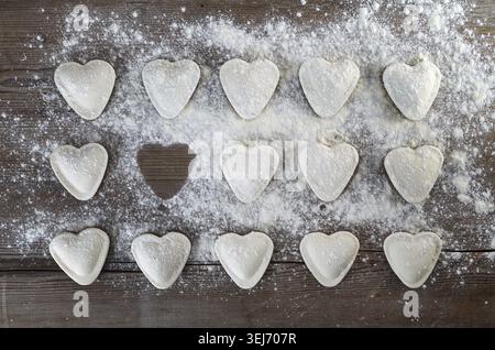 Herzförmige Ravioli mit Mehl bestreuen, auf hölzernem Hintergrund. Ungekochte Ravioli-Herzen. Kochenknödel. Draufsicht Stockfoto