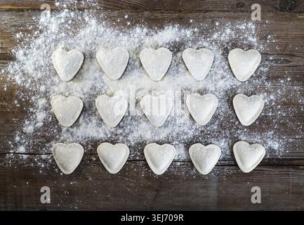 Herzförmige Ravioli mit Mehl, auf Vintage-Holztisch Hintergrund. Kochenknödel. Draufsicht Stockfoto