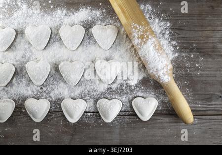 Kochenknödel. Rohe herzförmige Klöße, Mehl und Nudel auf hölzernem Hintergrund. Draufsicht Stockfoto